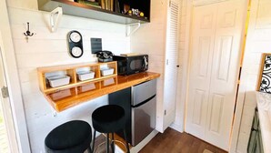 Una cocina compacta con encimera de madera, microondas, refrigerador y un taburete pequeño.