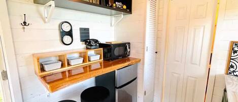 Una cocina compacta con encimera de madera, microondas, refrigerador y un taburete pequeño.