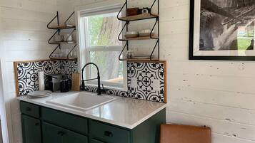 Una cocina con un lavamanos doble, gabinetes verdes y un salpicadero con estampado blanco y negro.