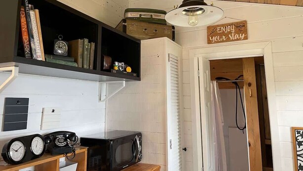 Una cocina compacta con un microondas antiguo, un reloj y una estantería con libros y una cámara.