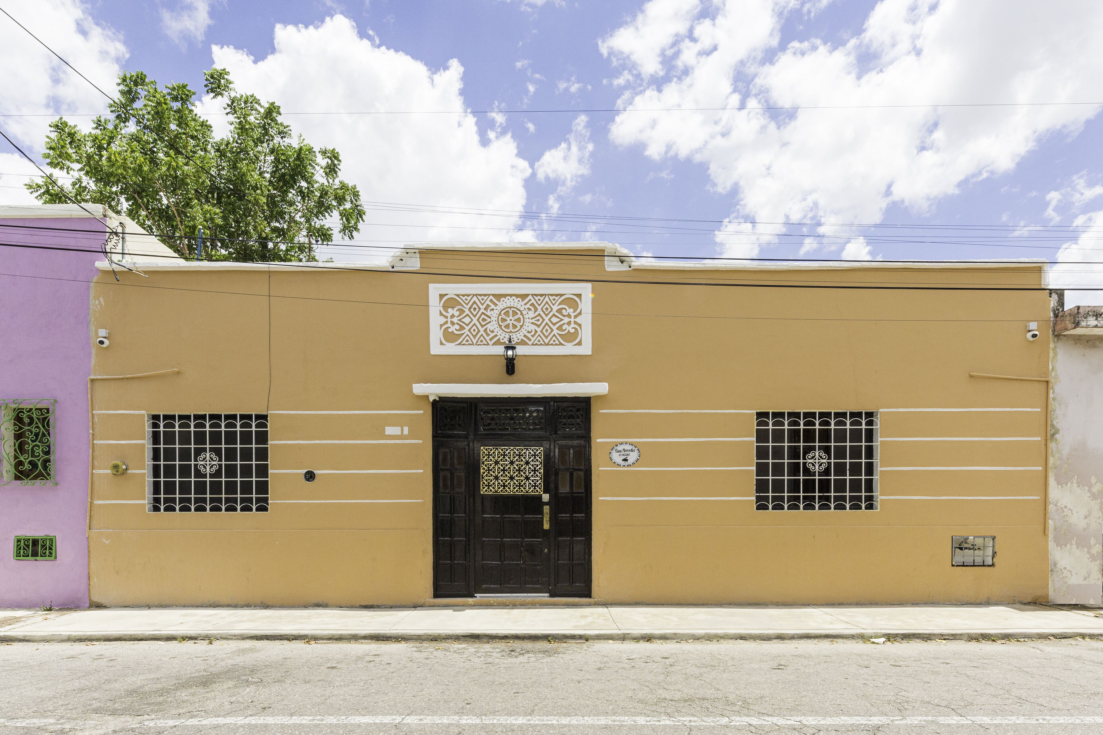 A building with a black door, two windows with metal bars, and a decorative sign above the door.