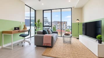 Ein modernes Wohnzimmer mit Sofa, Schreibtisch, Fernseher und Blick auf die Stadt.