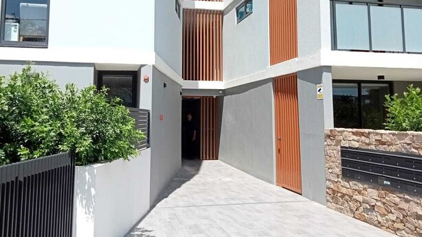 A modern multi-story building with a central courtyard, featuring a mix of white and wooden paneling, and a stone wall with mail slots. - KULA - Apartment Parramatta (Mays Hill)
