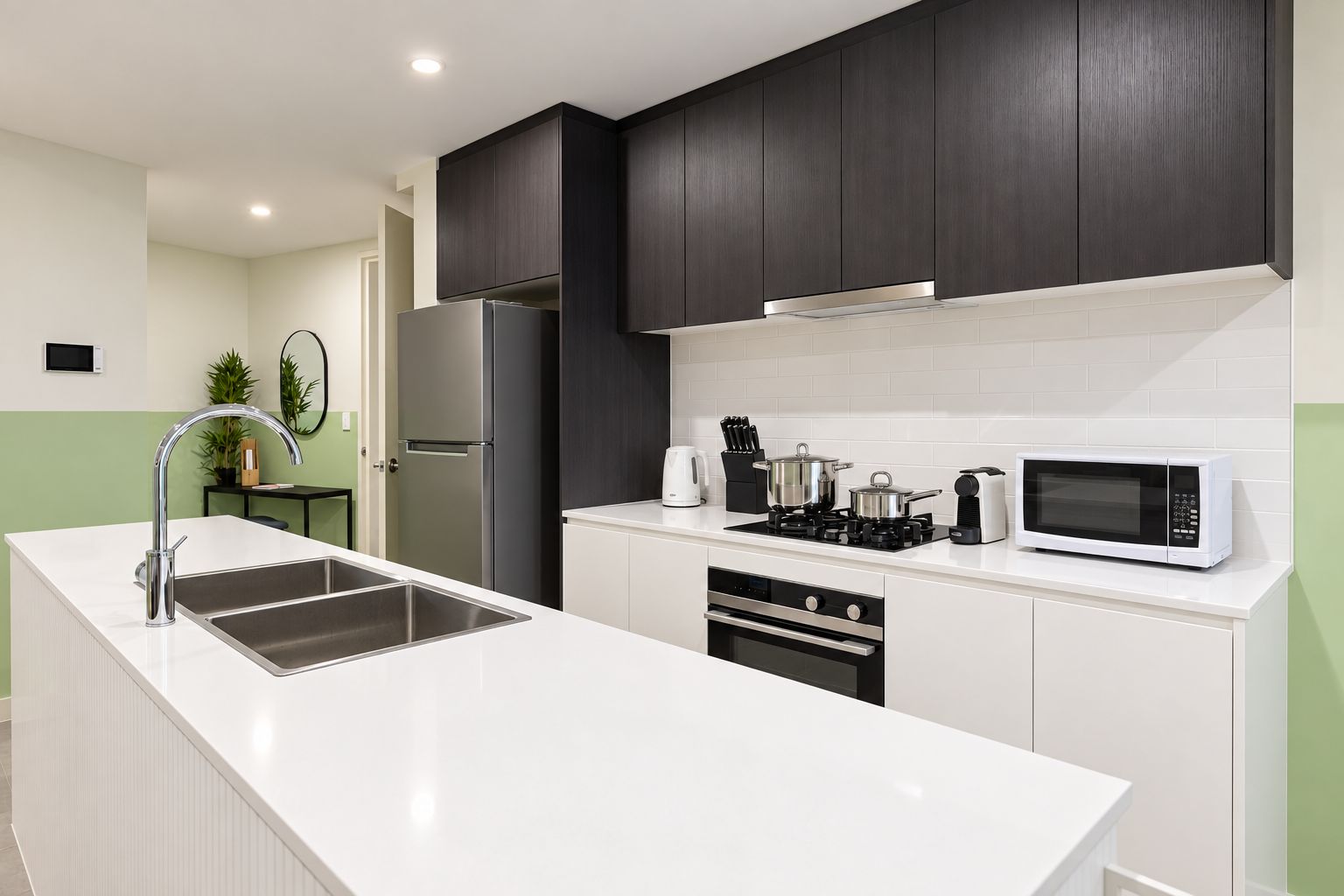 Une cuisine moderne dotée d’un îlot central, d’appareils électroménagers en acier inoxydable et de meubles de rangement aux couleurs sombres.