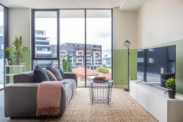 Una sala de estar moderna con un sofá, una mesita redonda, una lámpara de pie y un ventanal con vistas a edificios.