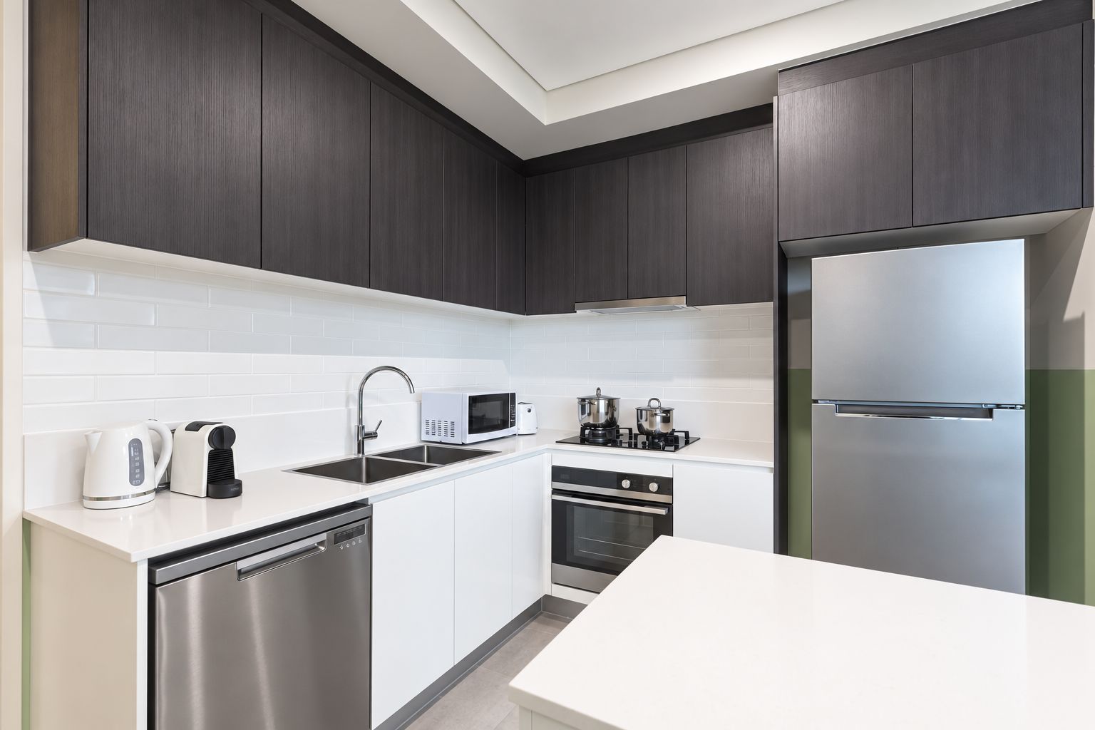 A modern kitchen with dark cabinets, white countertops, stainless steel appliances, and a dishwasher.