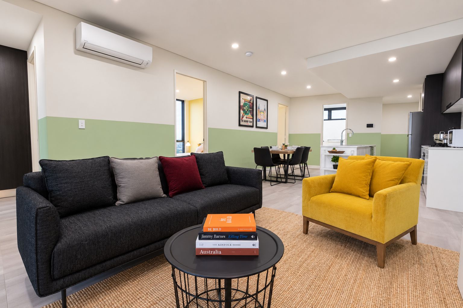 A modern living room with a sofa, a yellow armchair, a dining area, and a kitchenette.