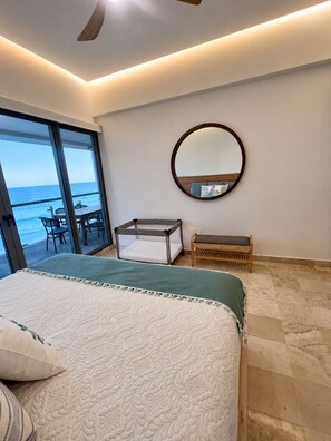 Una camera da letto con un letto grande, uno specchio rotondo, una panca e vista sull'oceano tramite una porta scorrevole.
