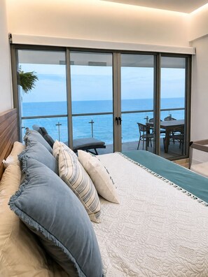 A bedroom with a large sliding glass door leading to a balcony with a view of the sea.