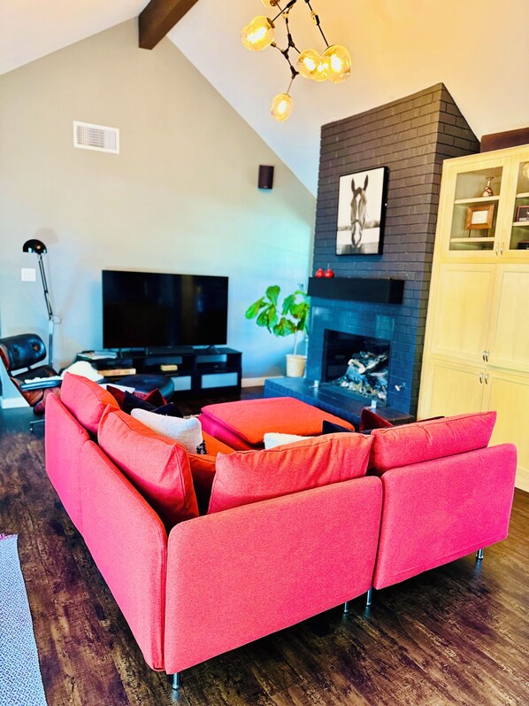 A living room with a red sofa, a fireplace, a television, and a plant. - Full House, Fire Place, BBQ, Private Pool and Backayrd in a Prime Location (Austin)