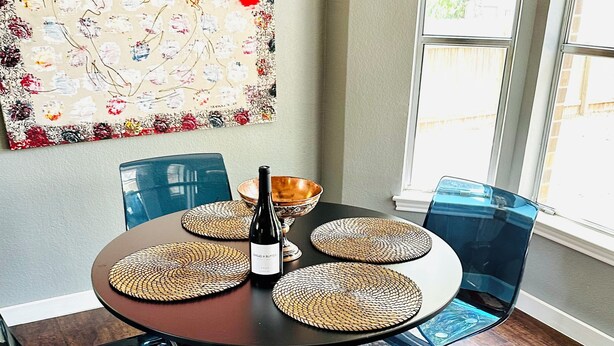 A modern dining area with a round table, black chairs, woven placemats, and a bottle of wine.