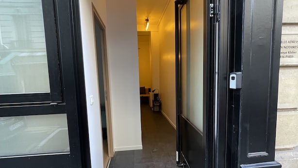 L’entrée d’un hôtel, avec une porte noire, un paillasson et un couloir menant à une chambre.