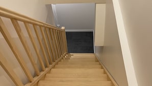 Un escalier en bois, avec des contremarches noires, menant à un palier.