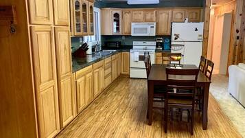 A kitchen with wooden cabinets, a dining table with chairs, a microwave, a refrigerator, and a stove.