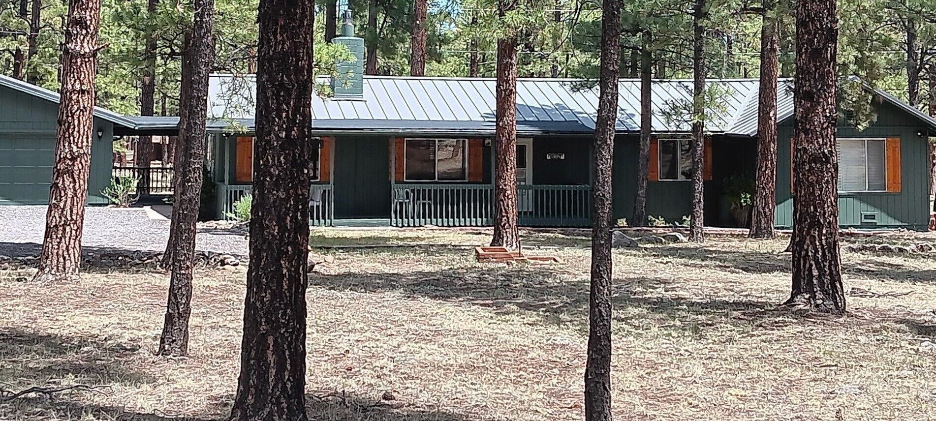 A cabin with a metal roof, surrounded by trees, and a small porch with a railing.