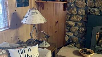A cozy cabin interior with wooden walls, a stone fireplace, a bear decoration, a lamp, and a cushion with a cabin-themed message.