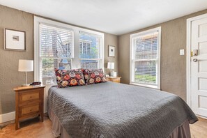 Une chambre à coucher avec un grand lit, deux tables de chevet, une commode et une fenêtre avec des stores.