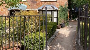 A stone house with a gated entrance, a covered porch, and a pathway leading to the door.