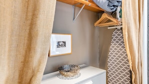 A neatly organized closet with hanging clothes, a framed picture on the wall, and a decorative bowl on a dresser.
