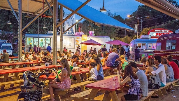 An outdoor dining area with picnic tables and umbrellas, surrounded by a metal structure.