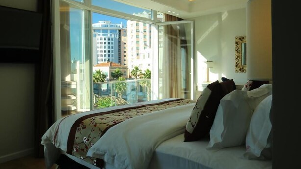 A hotel room with a large bed, a view of a cityscape through a sliding glass door, and a balcony with a pool. - Vila Brais (Durrës)