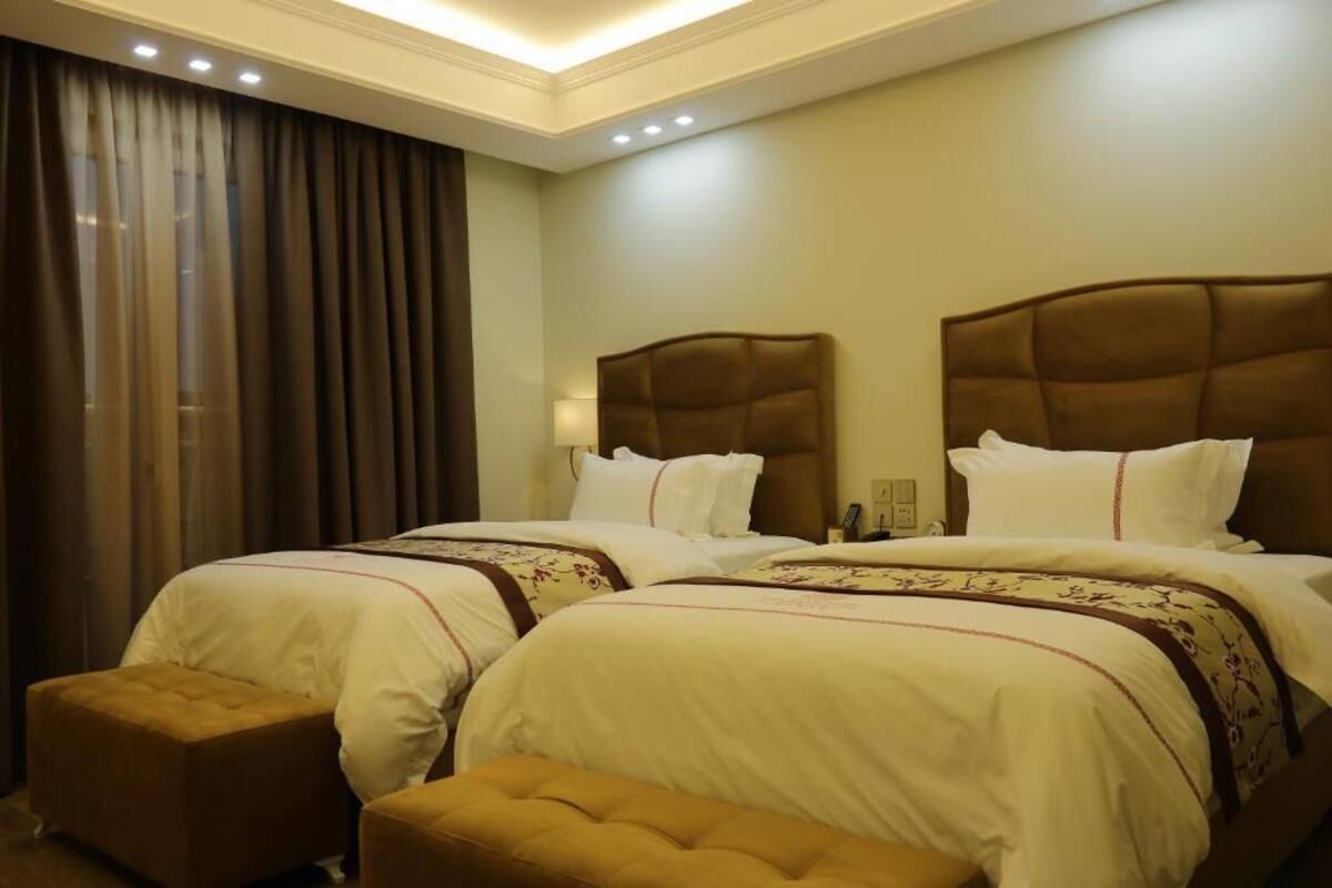 Ein Hotelzimmer mit zwei Betten, einem großen Fenster mit Vorhängen und einem kleinen Tisch.