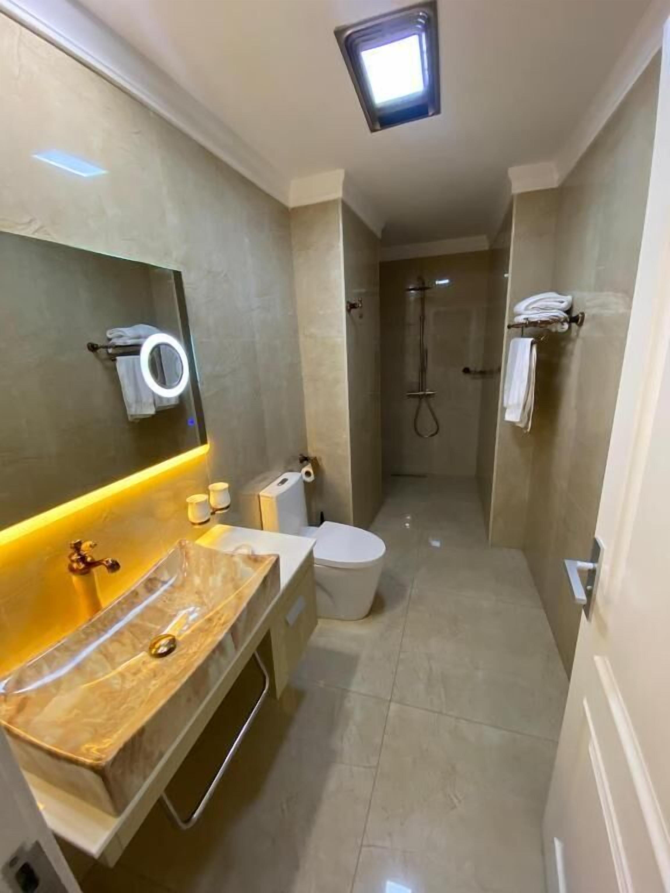Ein modernes Badezimmer mit Marmorwaschtisch, Toilette, Dusche und einem beleuchteten Spiegel.