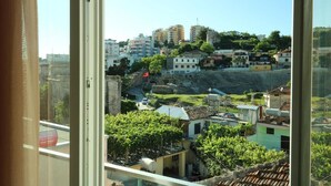 A view from a window overlooking a hillside with buildings, including a prominent red flag on a building. - Vila Brais (Durrës)