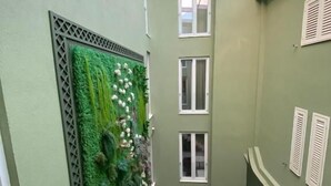 A narrow corridor with a green wall featuring a vertical garden and white flowers, leading to a seating area with tables and red chairs. - Vila Brais (Durrës)