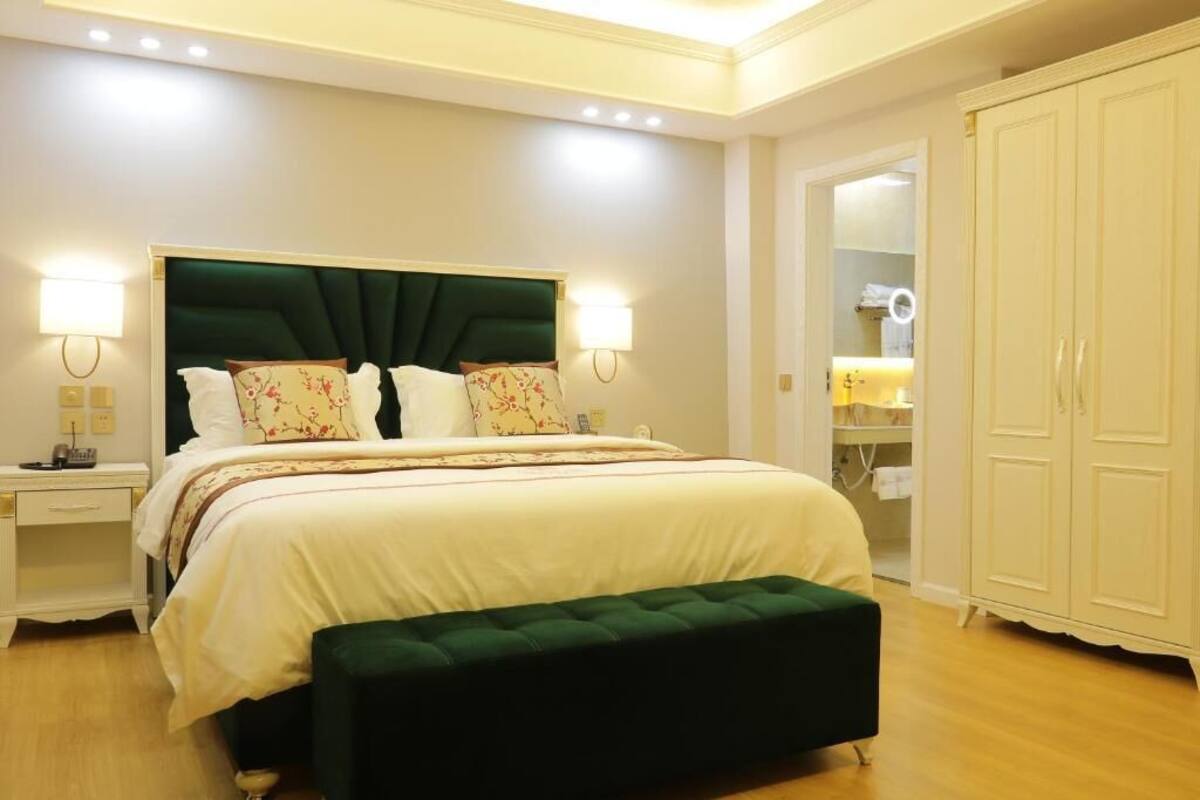 Ein ordentlich eingerichtetes Schlafzimmer mit einem großen Bett, Nachttischlampen, einer gepolsterten grünen Bank und einem Kleiderschrank.