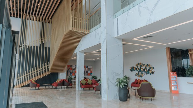 A modern lobby with a wooden slatted ceiling, marble flooring, and a seating area with red sofas and potted plants. - YE'S APART ASTANA (Astana)