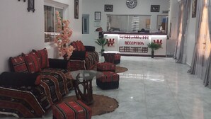 A reception area with a reception desk, a clock, and a sofa with patterned cushions. - Winbel Hotel (Hassi Messaoud)