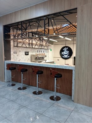 A modern bar area with a wooden counter, metal stools, and a coffee machine. - Winbel Hotel (Hassi Messaoud)