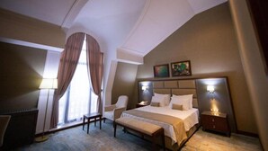 A hotel room with a large bed, a desk, a chair, and a window with curtains.