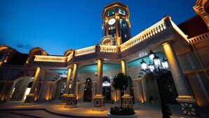 A grand hotel with a clock tower, arched walkways, and a well-lit facade.