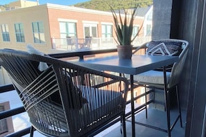 Un balcone con mobili in vimini, una pianta in vaso e vista sugli edifici.