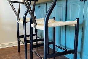 Una cucina con mobili color petrolio e una sedia in metallo nero con seduta intrecciata.