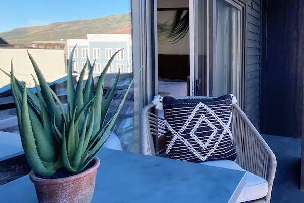 A balcony with a potted plant, a wicker chair with a patterned pillow, and a view of buildings in the background. - Studio 580 Main (Park City)