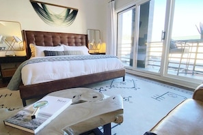 A hotel room with a large bed, a wooden side table, a book, and a view of the outside through a sliding door. - Studio 580 Main (Park City)