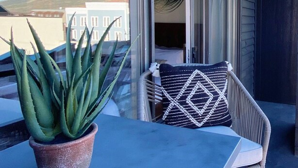 A balcony with a potted agave plant, a wicker chair with a patterned cushion, and a view of buildings in the background. - Labor Day Sale - Limited Time Offer, Save up to 30% (Park City)
