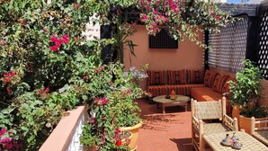A cozy outdoor seating area with a sofa and chairs, surrounded by lush greenery and flowering plants. - Surf Riad in Taghazout (Taghazout)