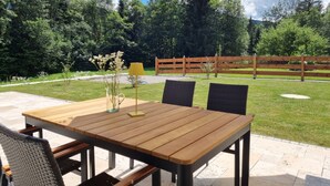 Eine Terrasse im Freien mit einem Holztisch und Stühlen, einem gestreiften Sonnenschirm und einer Vase mit Blumen.