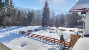 Schneebedeckte Landschaft mit Holzzaun, kleinem Baum und Gebäude mit verschneitem Dach.