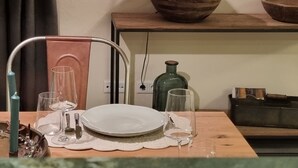 Ein Essbereich mit einem Holztisch, einem Metallhahn, klaren Gläsern, einem weißen Teller und einer grünen Flasche.