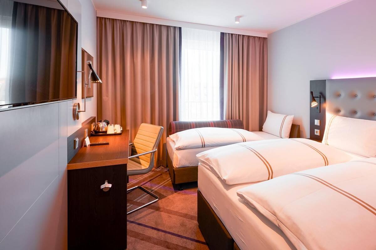 A hotel room with two beds, a desk, a chair, a TV, and a window with curtains.