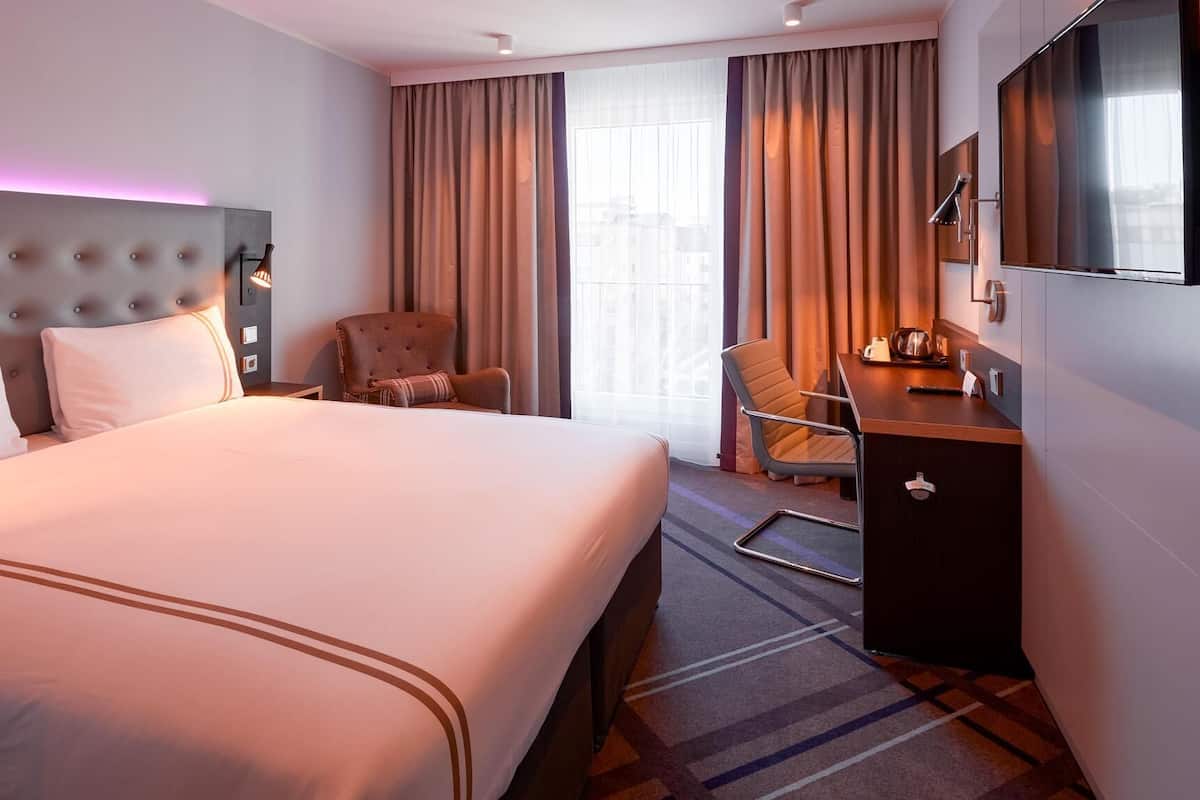 A hotel room with a large bed, a desk with a chair, a TV, and a window with curtains.