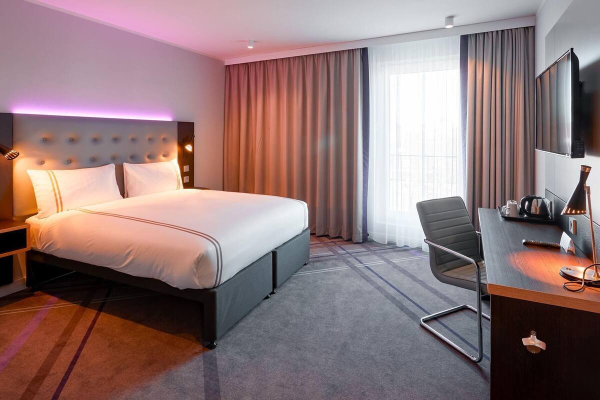 A hotel room with a bed, a desk, a chair, a TV, and a window with curtains.