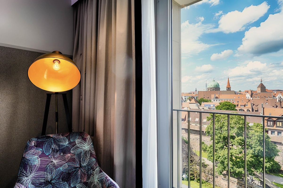 Una habitación con vistas a la ciudad, una lámpara, una silla y una ventana con cortinas.