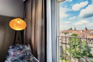 A room with a view of a cityscape, a lamp, a chair, and a window with curtains. - Premier Inn Nürnberg City Opernhaus (Nuremberg)