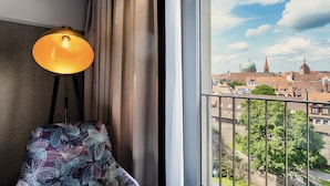 A room with a view of a cityscape, a lamp, a chair, and a window with curtains. - Premier Inn Nürnberg City Opernhaus (Nuremberg)